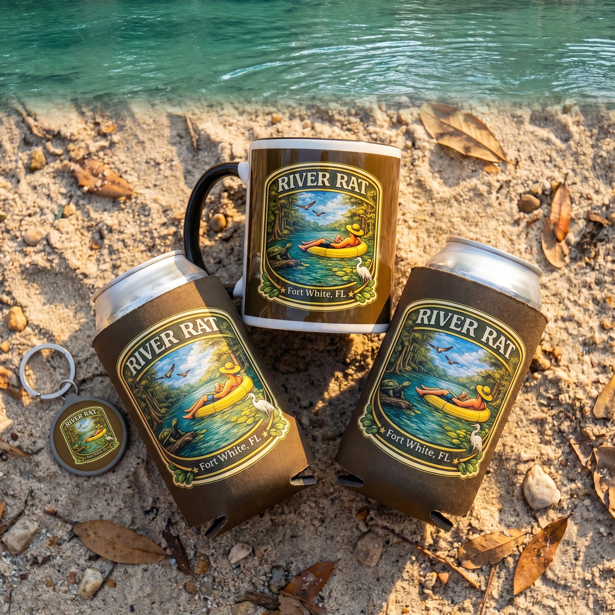 River Life Gift Bundle Mug Cozy Keyring flat-lay on sandy riverbank