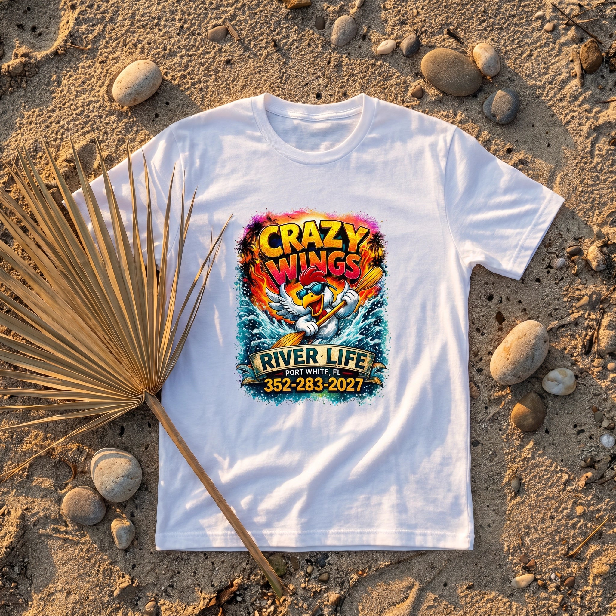 The Owen Mens T-Shirt Crazy Wings flat-lay on sandy riverbank