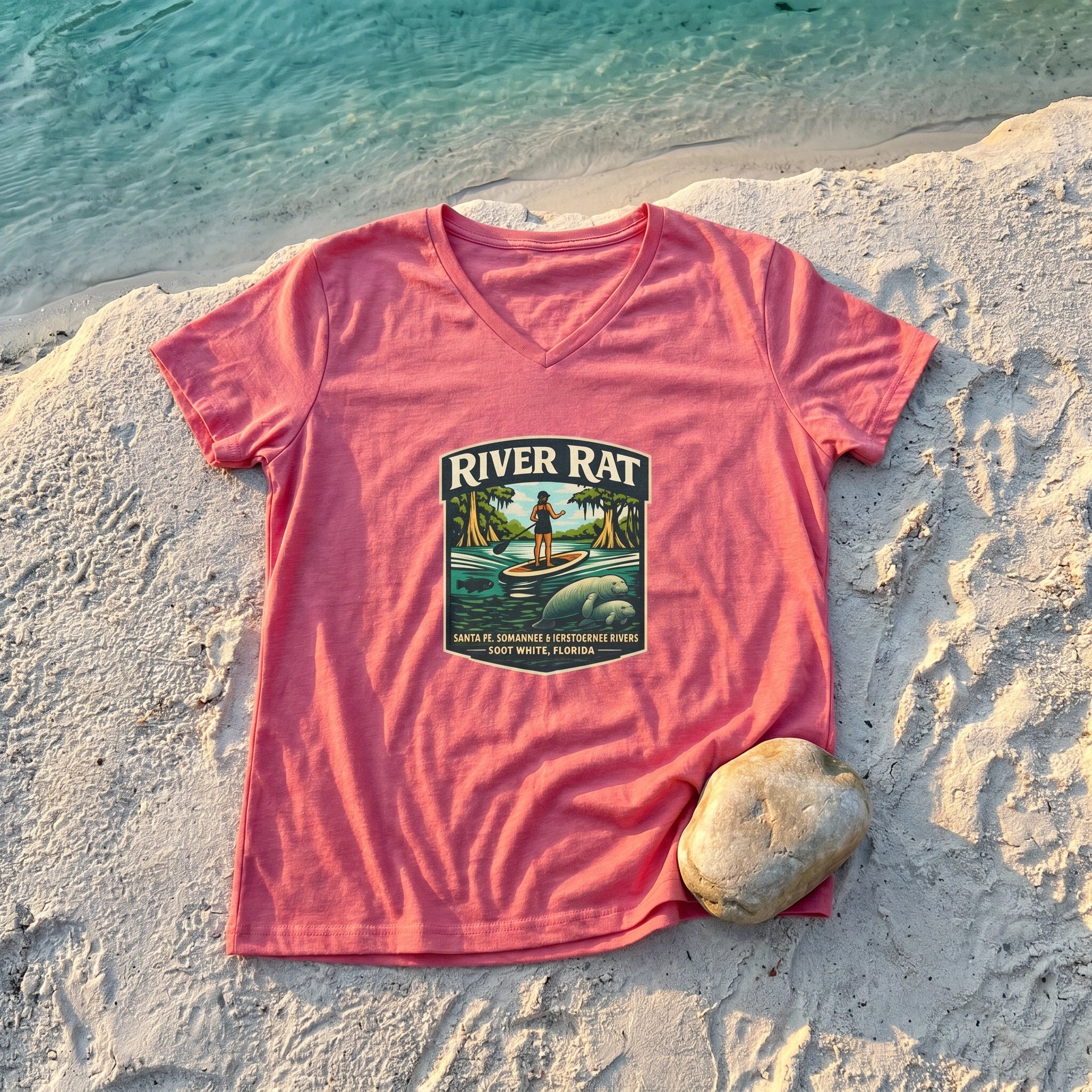 River Life Ladies Tee — flat-lay on sandy riverbank with river rock, turquoise spring water